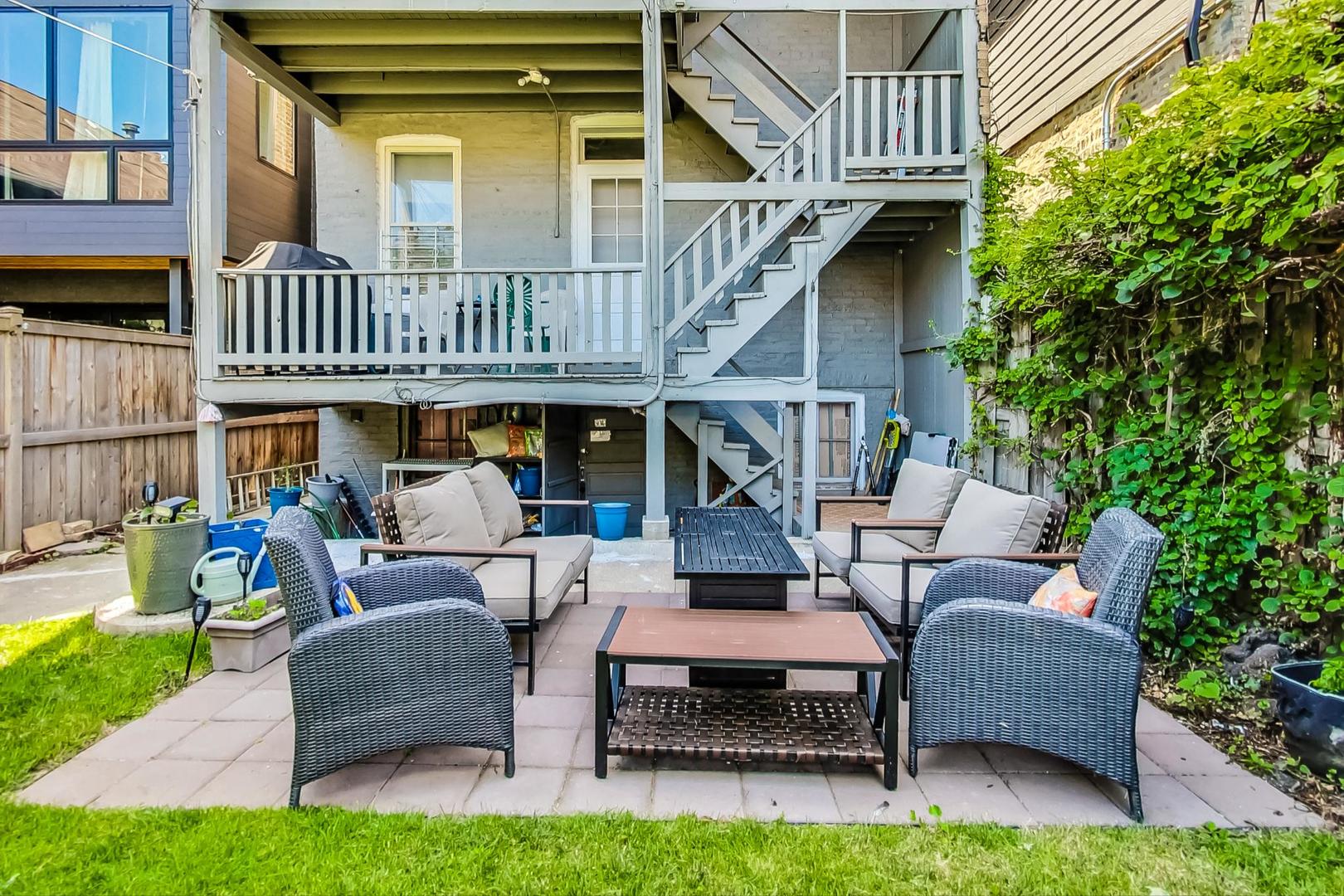 Backyard patio with wicker seating and coffee tables beneath a raised deck and exterior stairs.