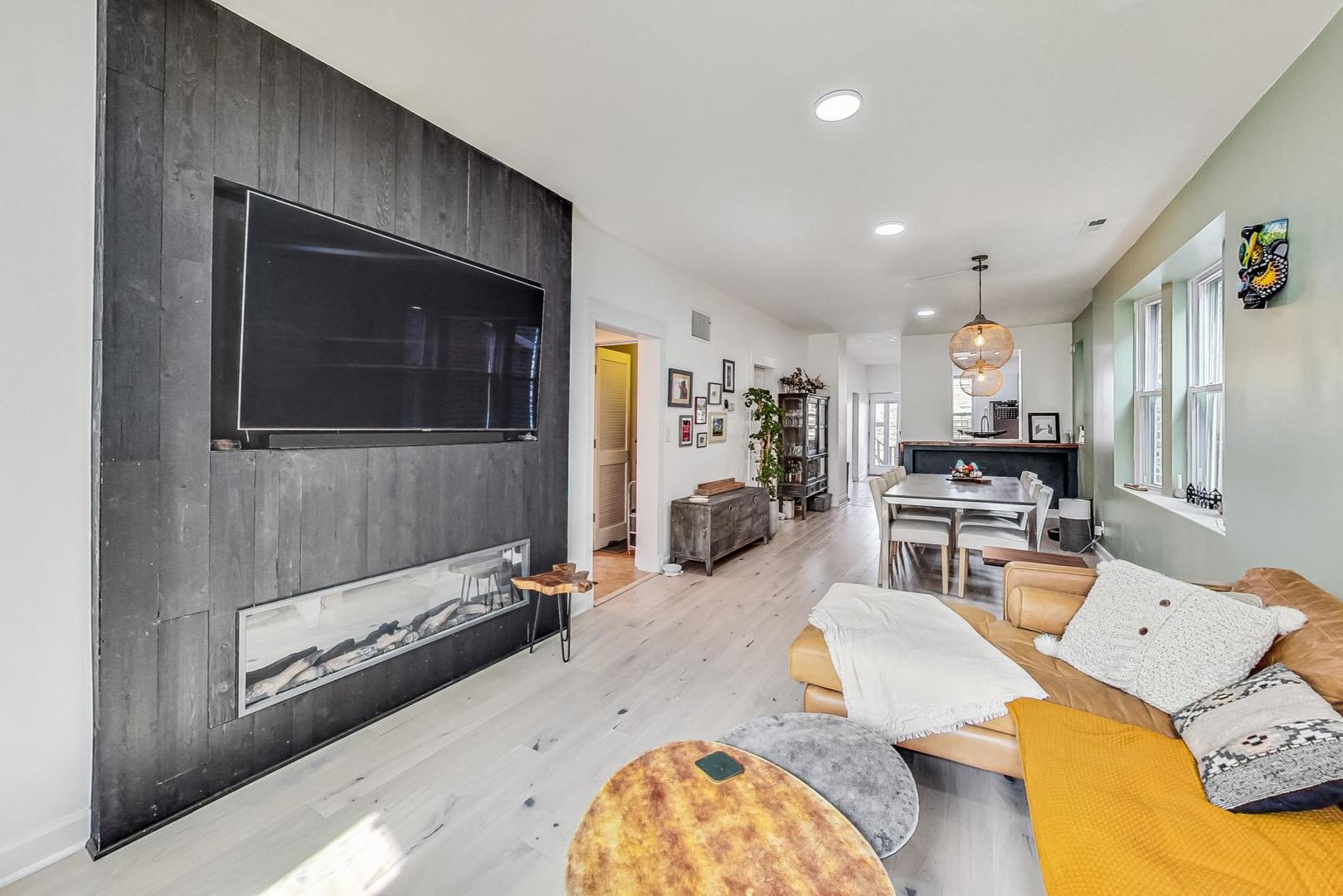 Living room with a dark paneled fireplace wall, tan sectional, and adjoining dining area.