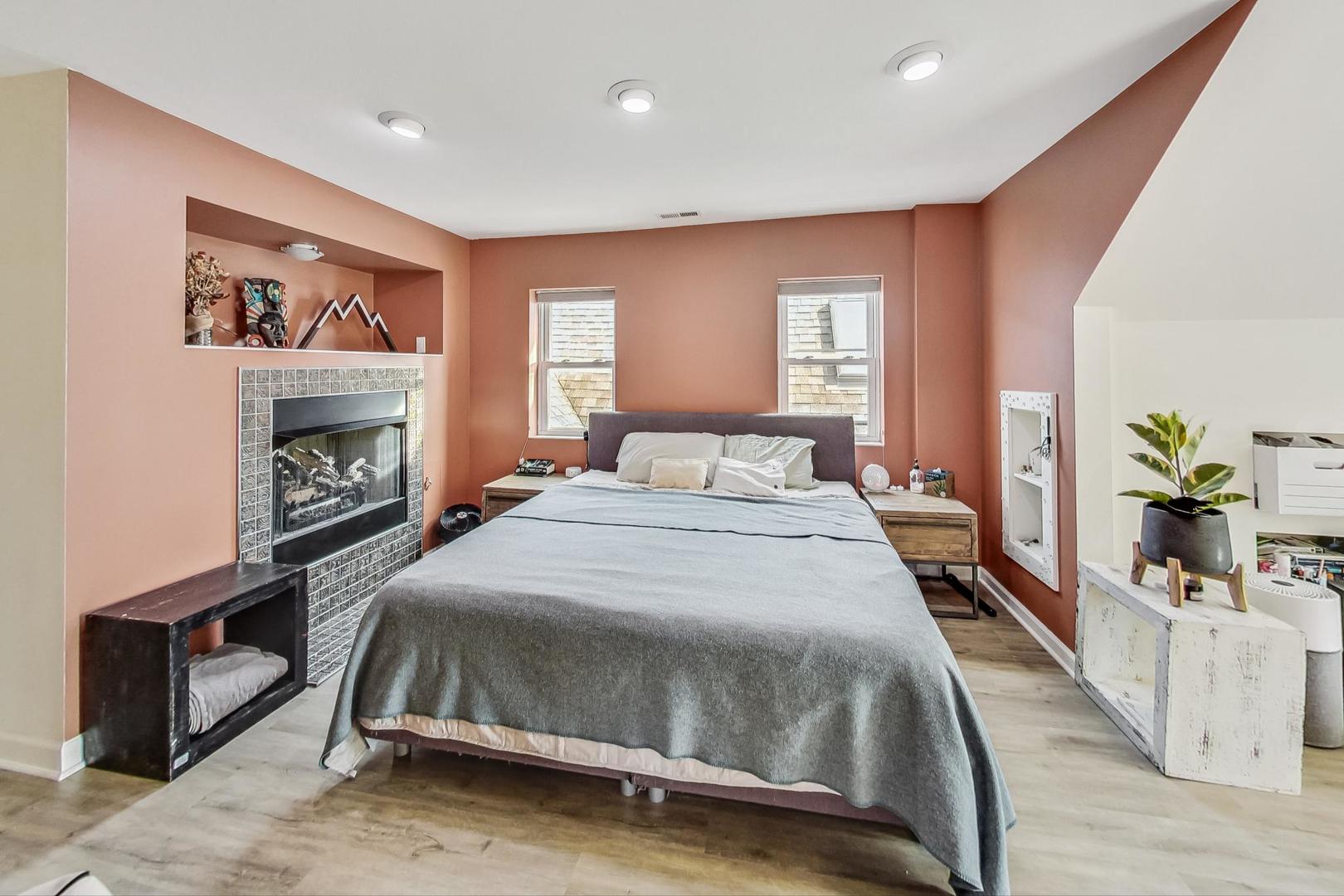 Staged bedroom with a large bed, tiled fireplace, and terracotta walls.