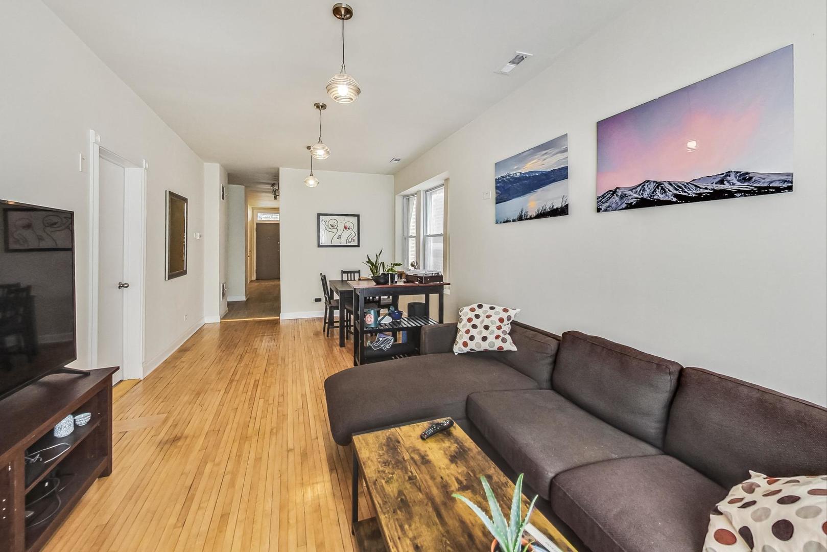 Living and dining area with hardwood floors, a dark sectional, and a dining table by the windows.