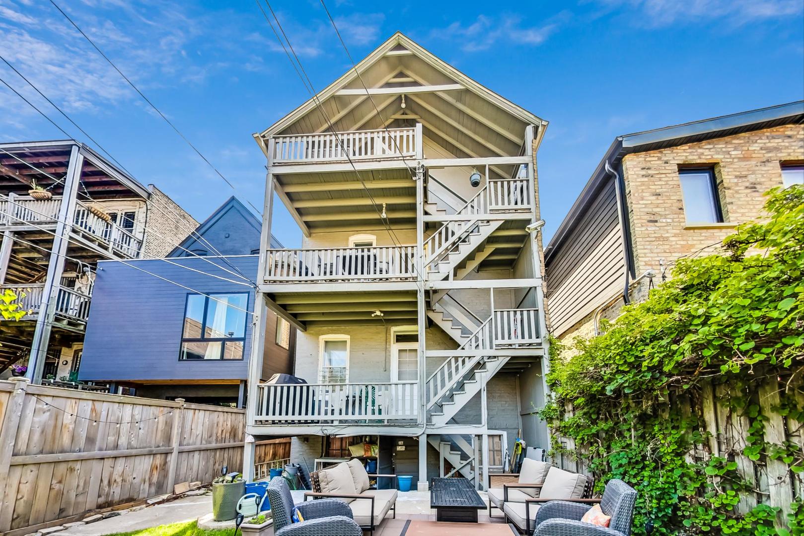 Home’s rear balconies and exterior stairs overlook a patio furnished with lounge chairs and a coffee table.