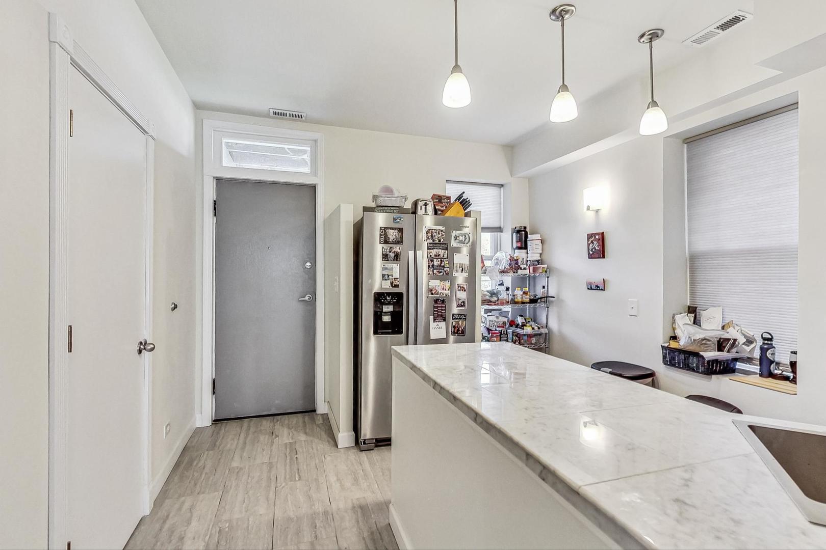 Kitchen with a long marble island, stainless steel refrigerator, and three pendant lights.