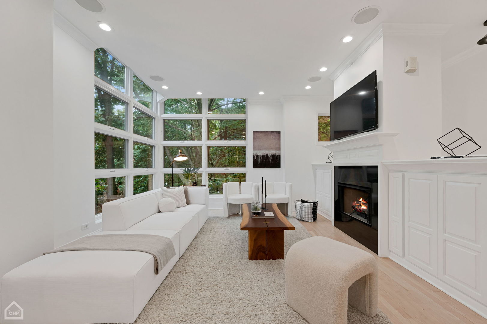 Living room with tall windows, white seating, and a lit fireplace.