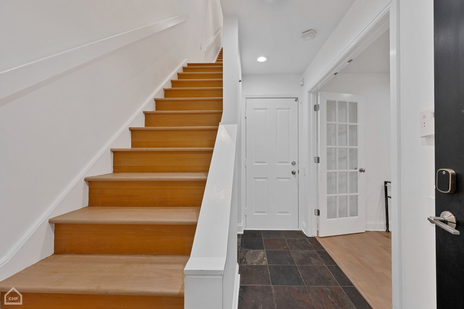 Entry hall with a wooden staircase, dark tile floor, and white front door.