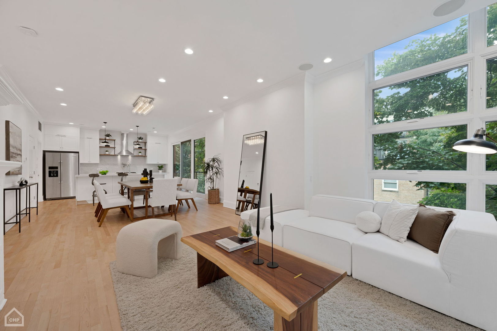 Open-plan living room with a white sectional, dining table, kitchen, and tall windows.