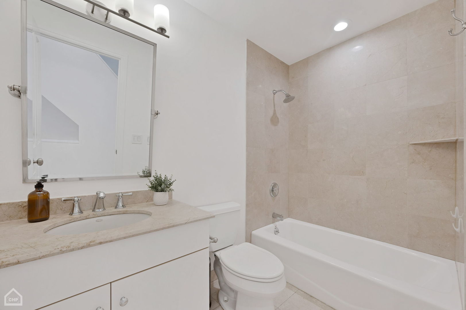Bathroom with a stone-tiled tub and shower beside a white vanity and large mirror.