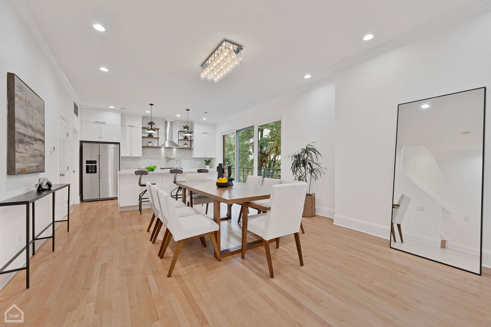 Open kitchen and dining area with white cabinetry, a wood table, and large windows overlooking trees.