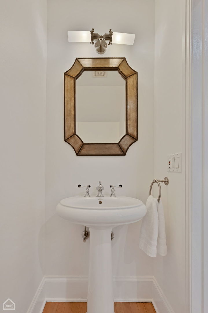 Powder room with a white pedestal sink, ornate wood-framed mirror, and towel ring.
