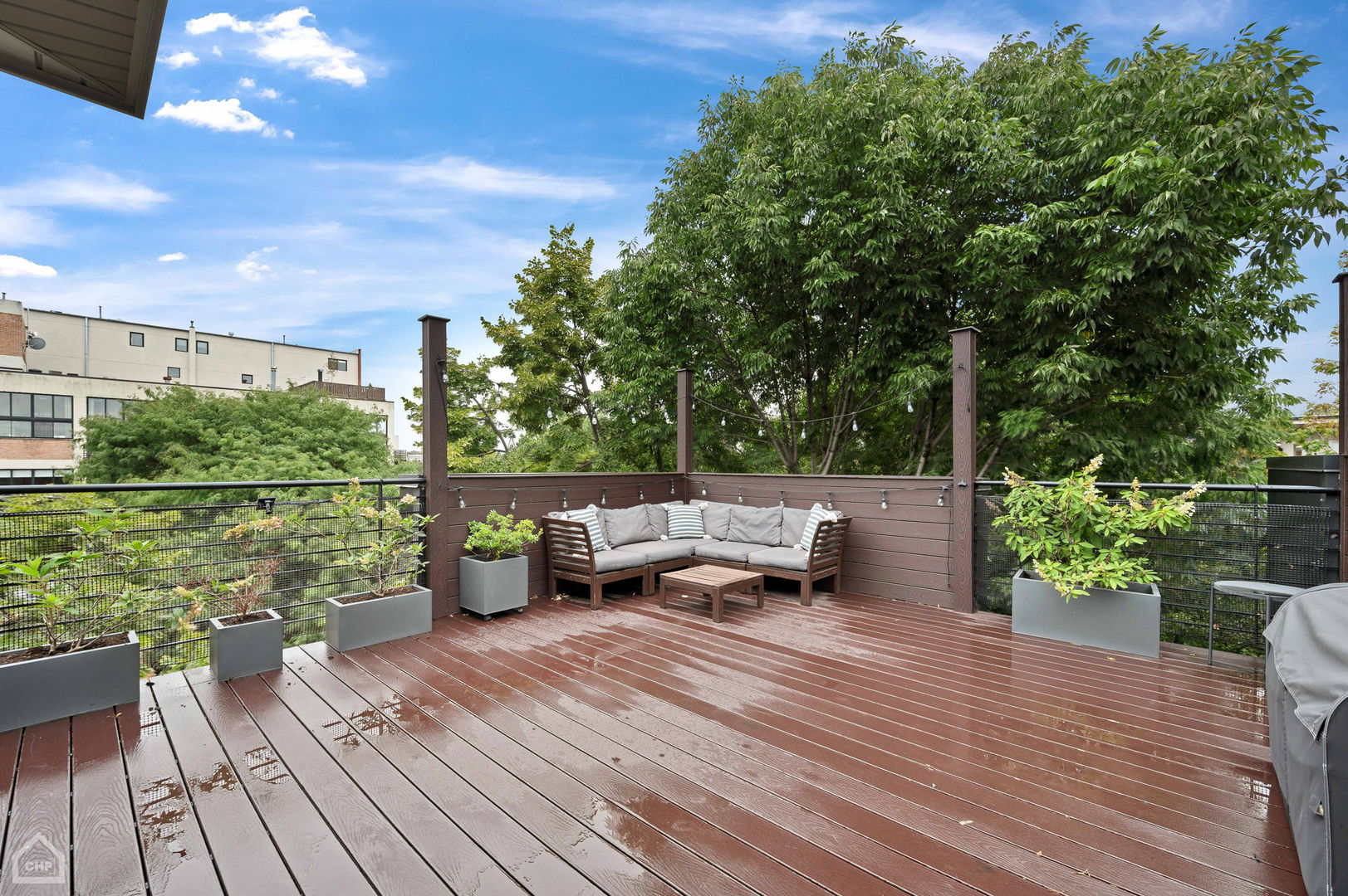 Rooftop deck with a cushioned sectional, raised planters, and mature trees beyond the railing.
