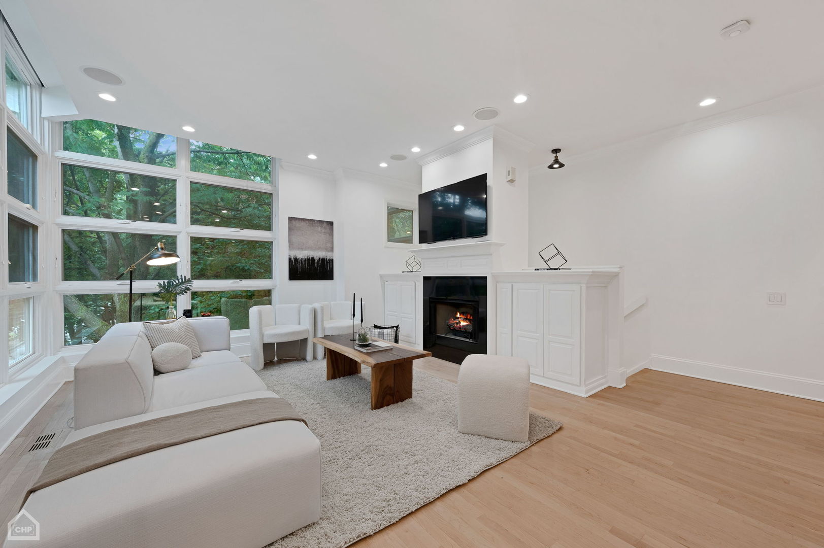 Living room with a white sectional, fireplace, and tall windows overlooking leafy trees.