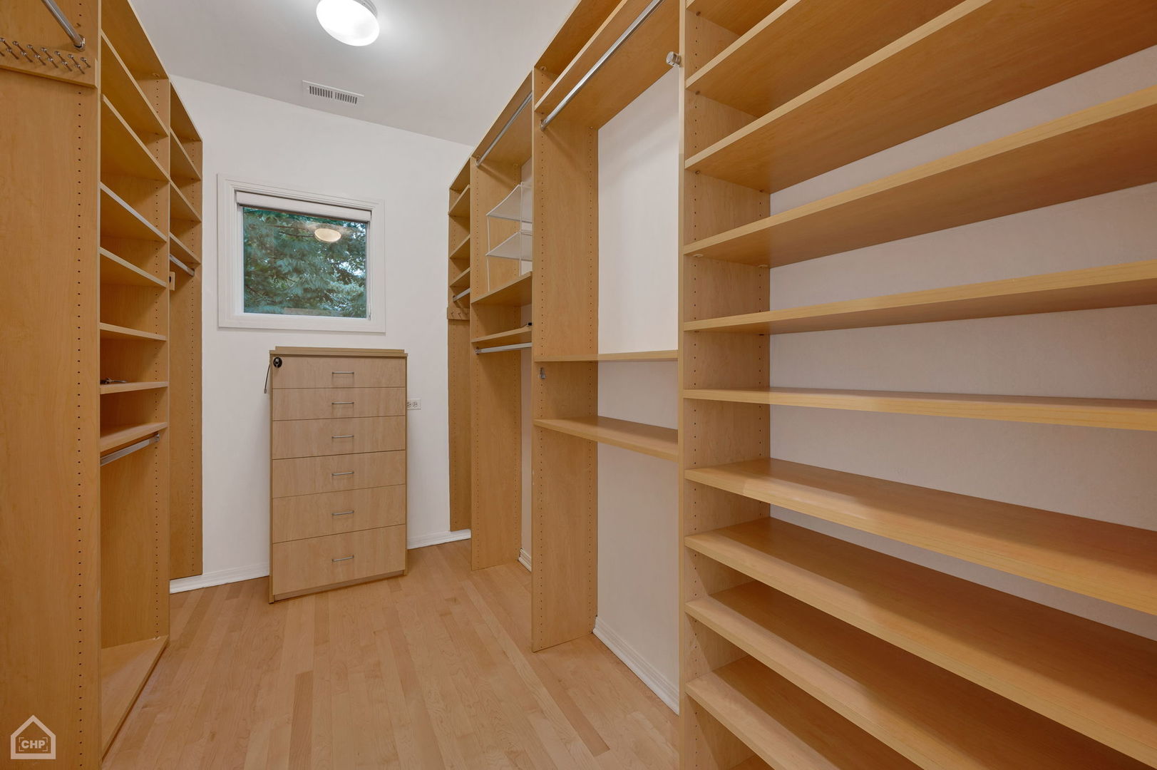 Walk-in closet with built-in wood shelving, hanging rods, and a matching chest of drawers.