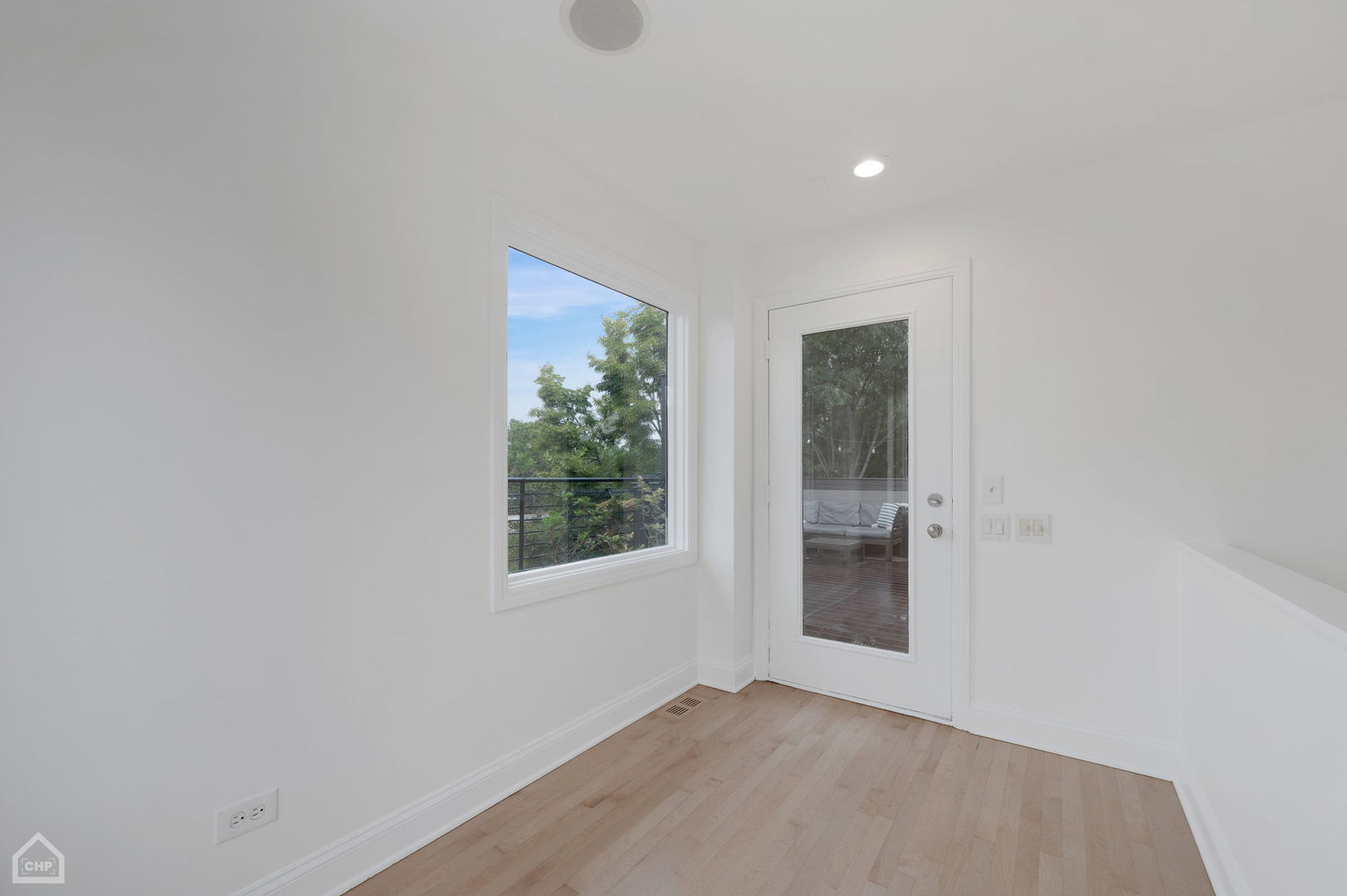 Vacant room with light hardwood floors, a large window, and a glass door to the deck.