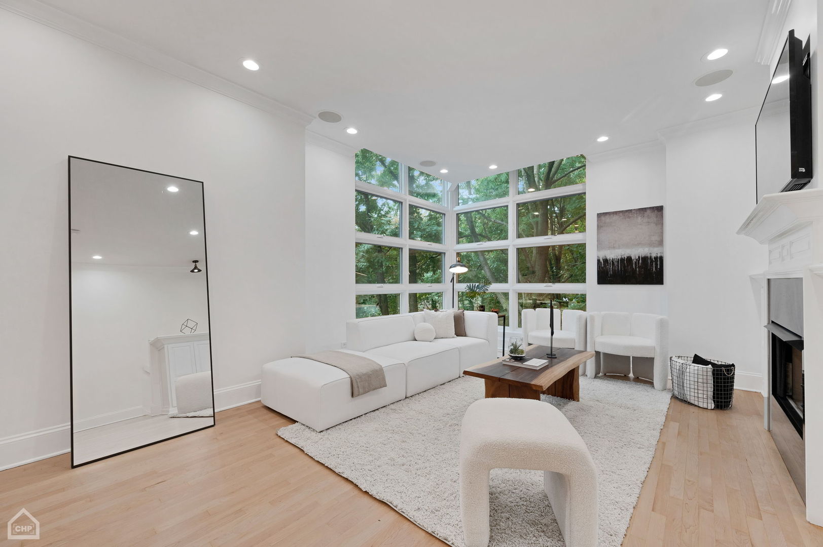 Living room with a white sectional, fireplace, and floor-to-ceiling windows overlooking trees.