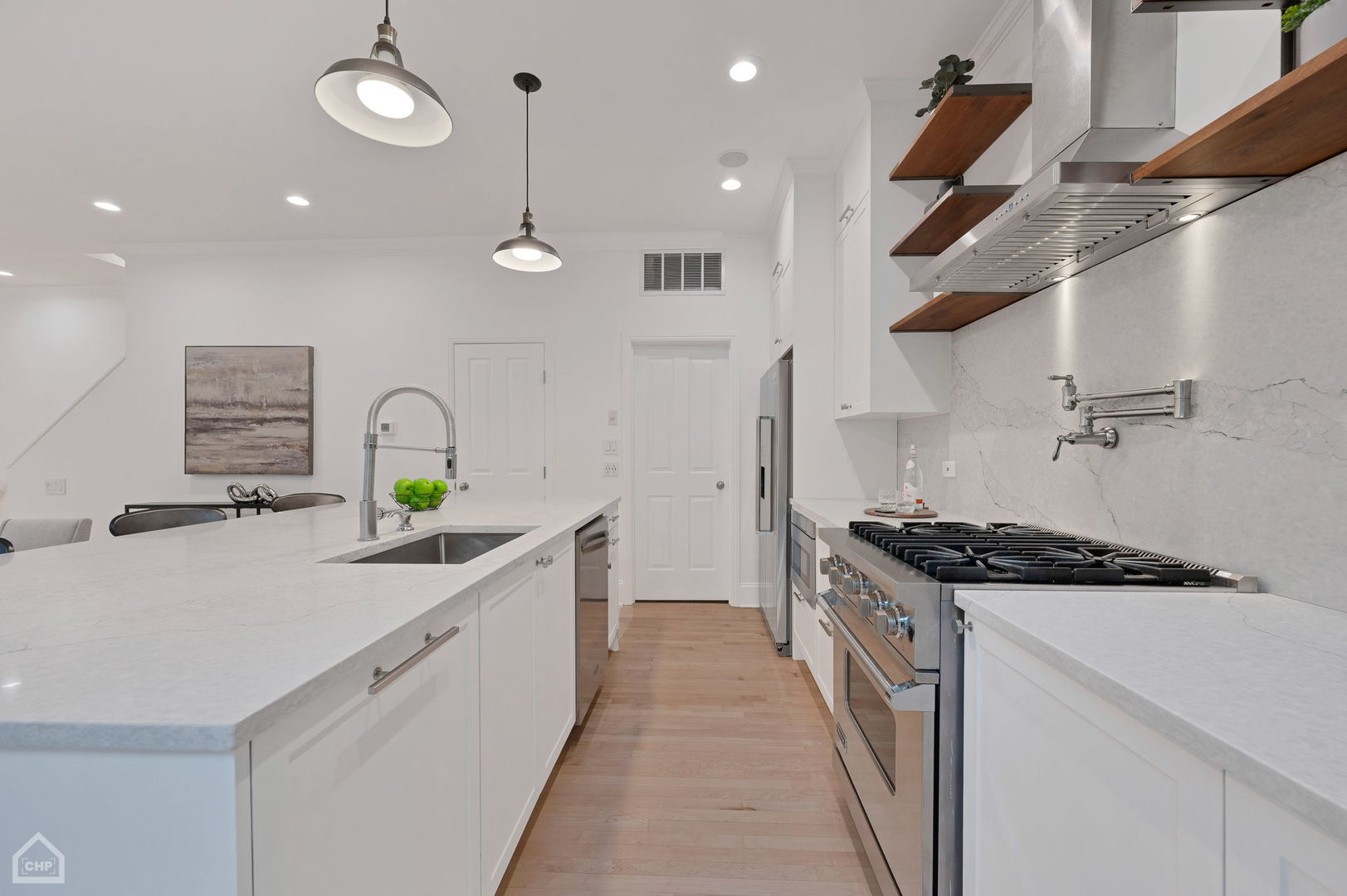 Modern white kitchen with a large island, pale stone counters, and a stainless steel gas range.