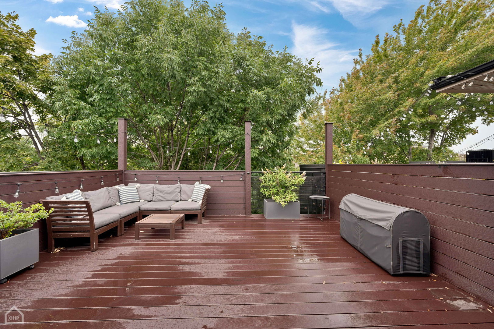 Wood deck with an outdoor sectional, string lights, and leafy trees beyond the privacy fence.