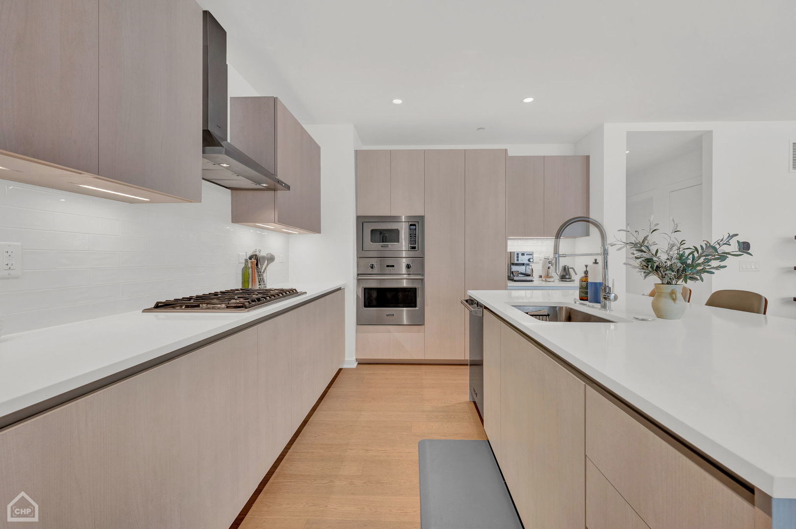 Modern condo kitchen with pale wood cabinetry, stainless appliances, and a large white island with sink.