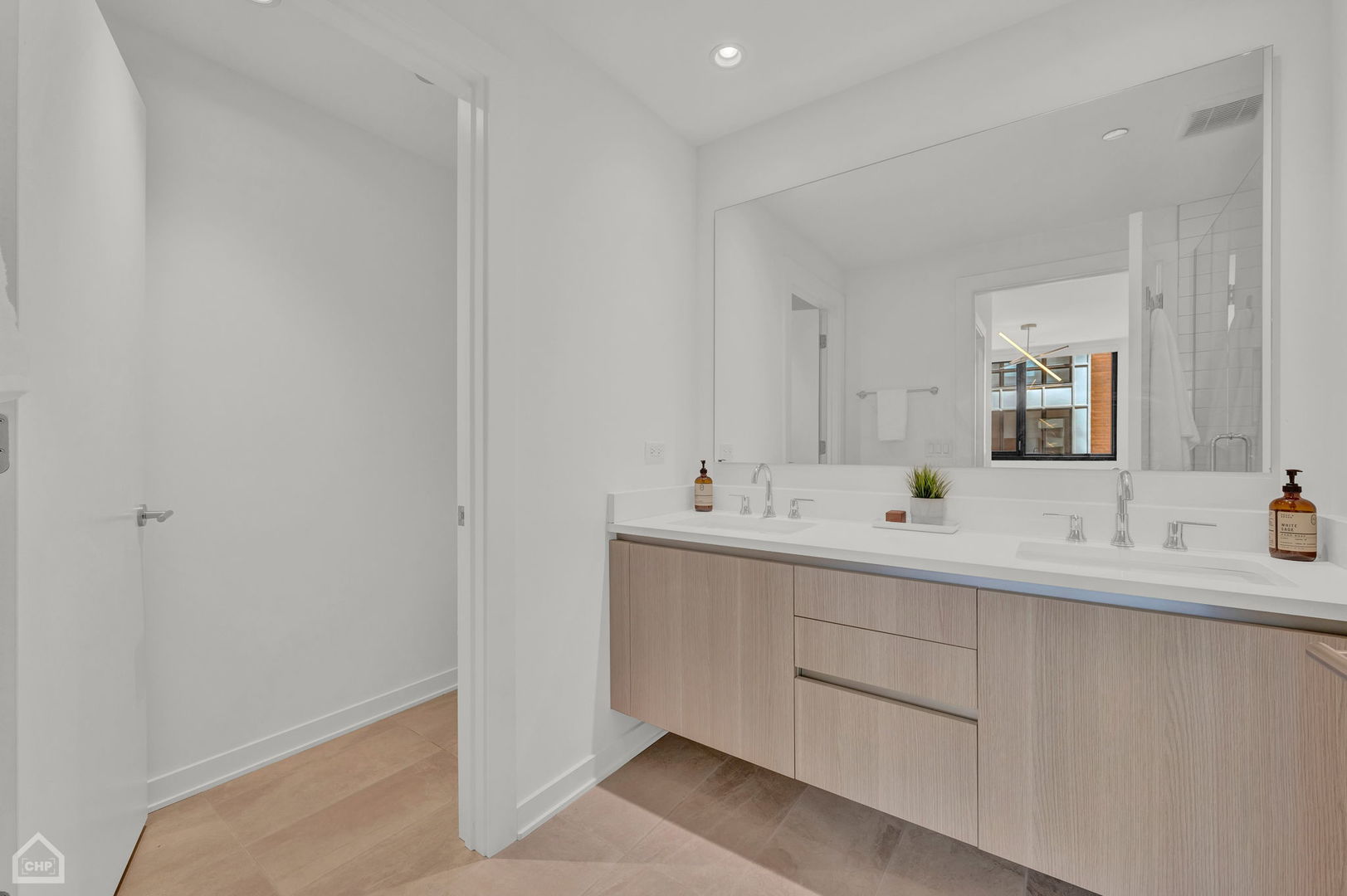 Modern bathroom with a light-wood double vanity, two sinks, and a large mirror reflecting the tiled shower.