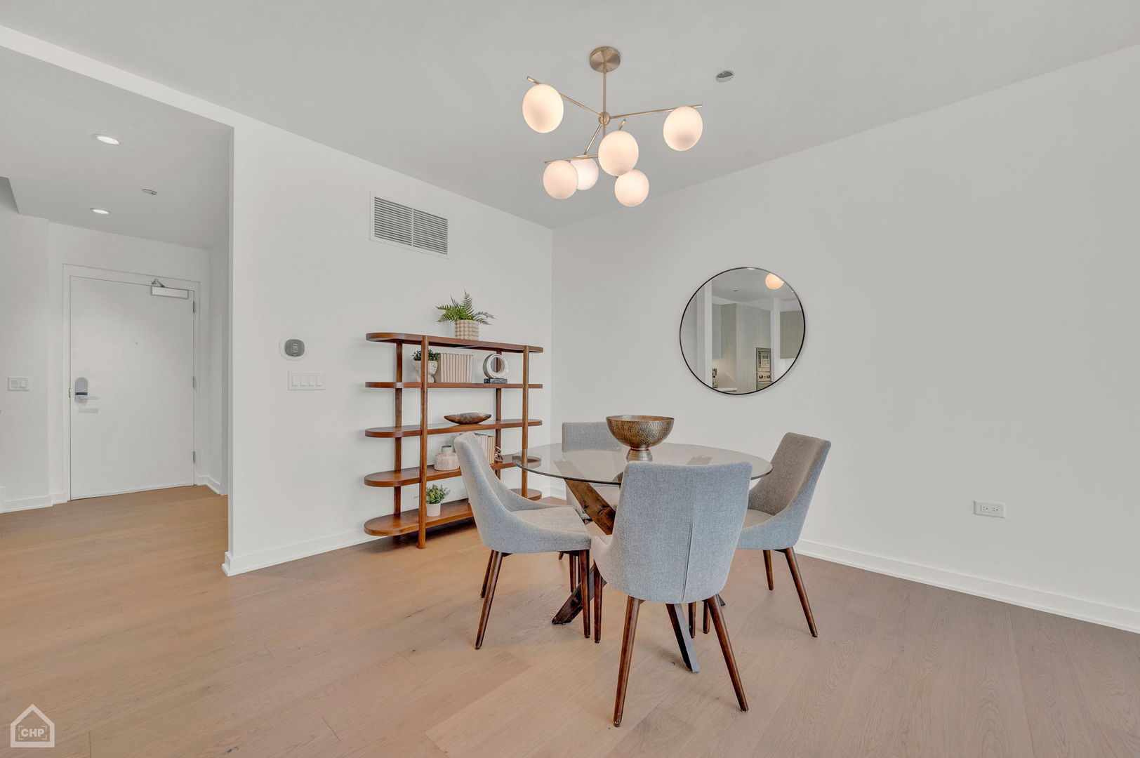 Dining area with a glass-top table, gray chairs, sculptural wood shelves, and a globe chandelier.