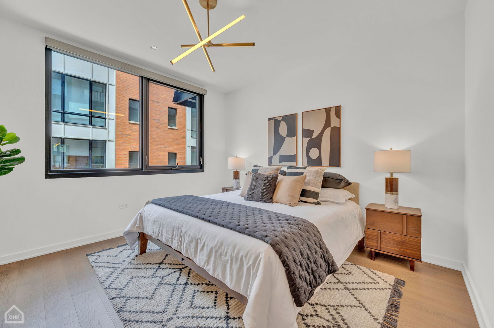 Staged bedroom with a king-size bed, modern pendant light, and large window overlooking a neighboring building.