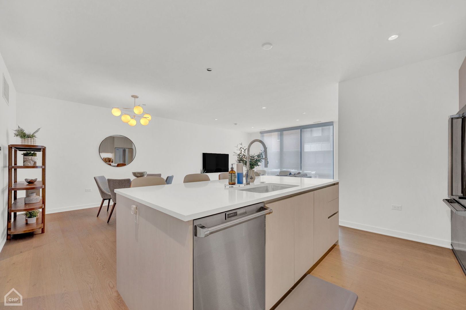 Open-plan kitchen with a large white island, stainless steel dishwasher, and pale wood floors.
