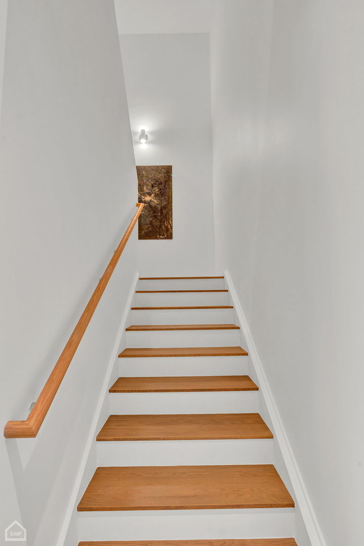 Staircase with warm wood treads and handrail, leading to a landing with artwork.