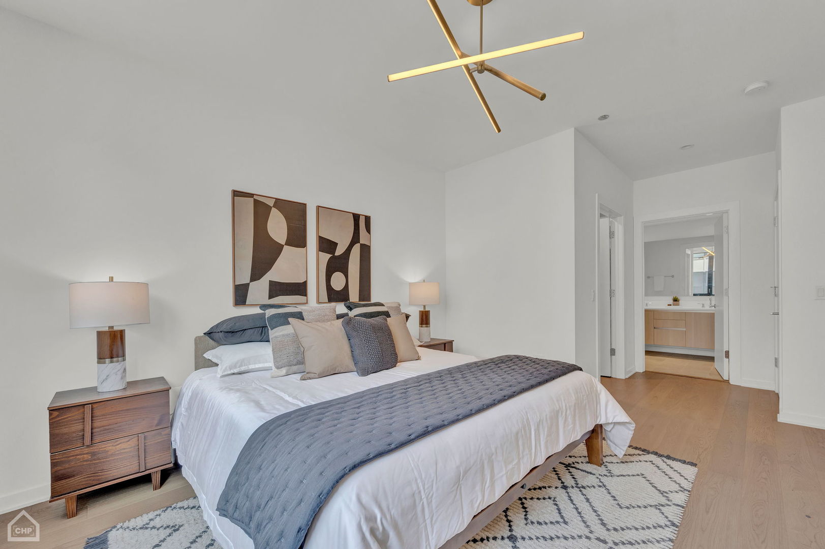 Staged bedroom with blue-gray bedding, abstract wall art, and an open doorway to the ensuite bathroom.