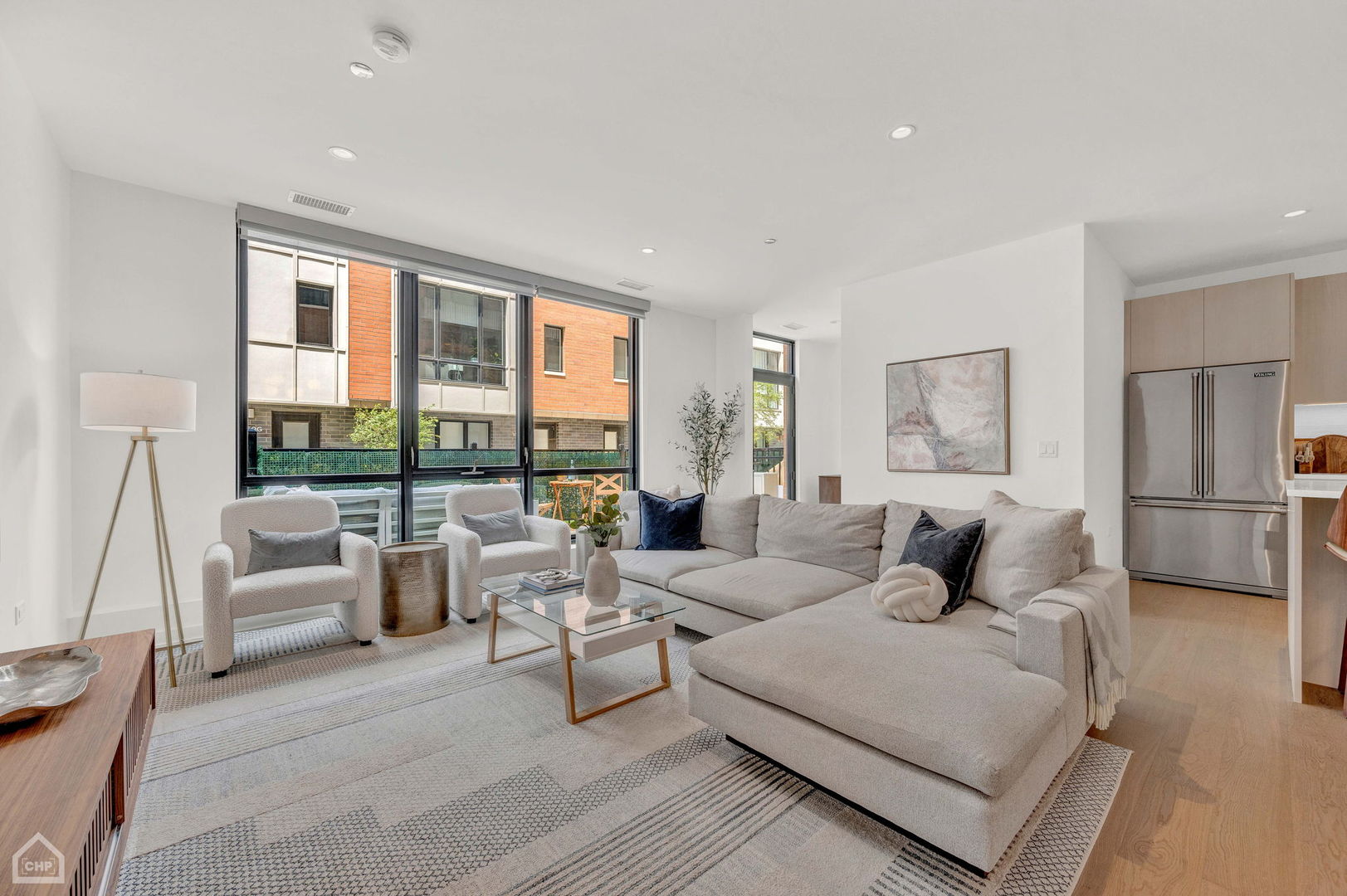 Staged living room with a large sectional sofa and floor-to-ceiling courtyard windows.