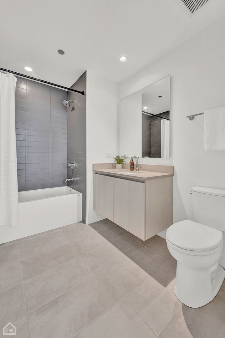 Modern bathroom with a gray-tiled tub and shower, floating wood vanity, large mirror, and white toilet.