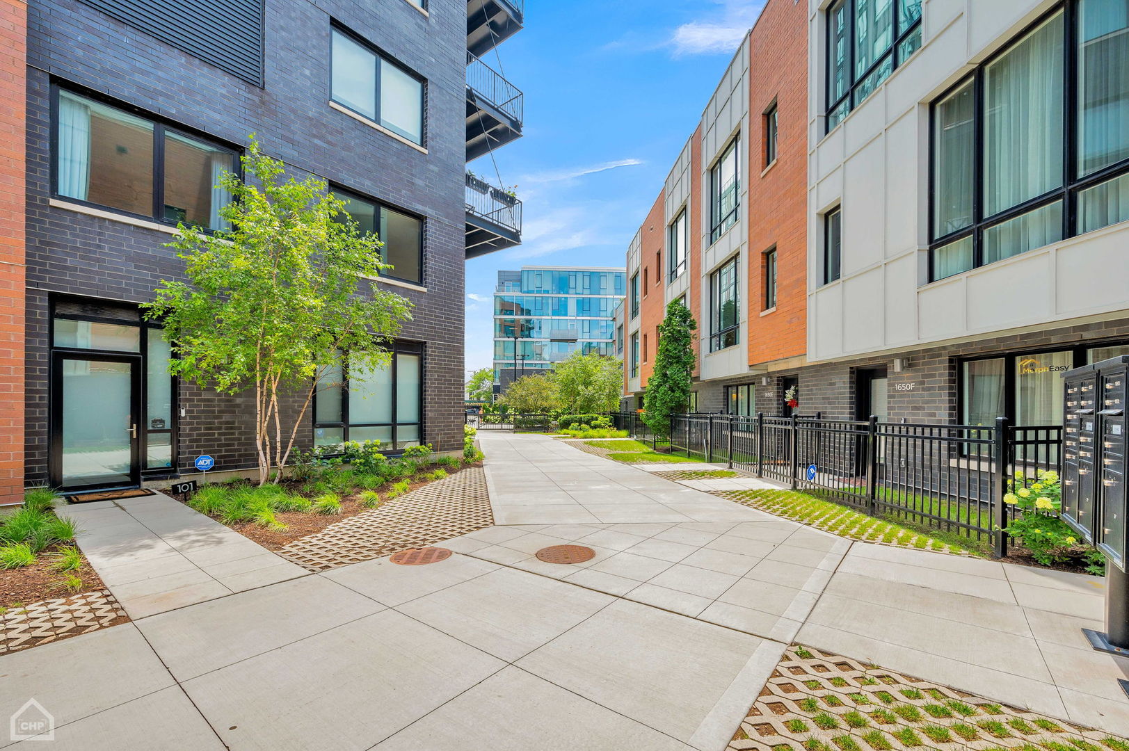 Paved courtyard between modern residential buildings, with landscaped beds and black metal railings.