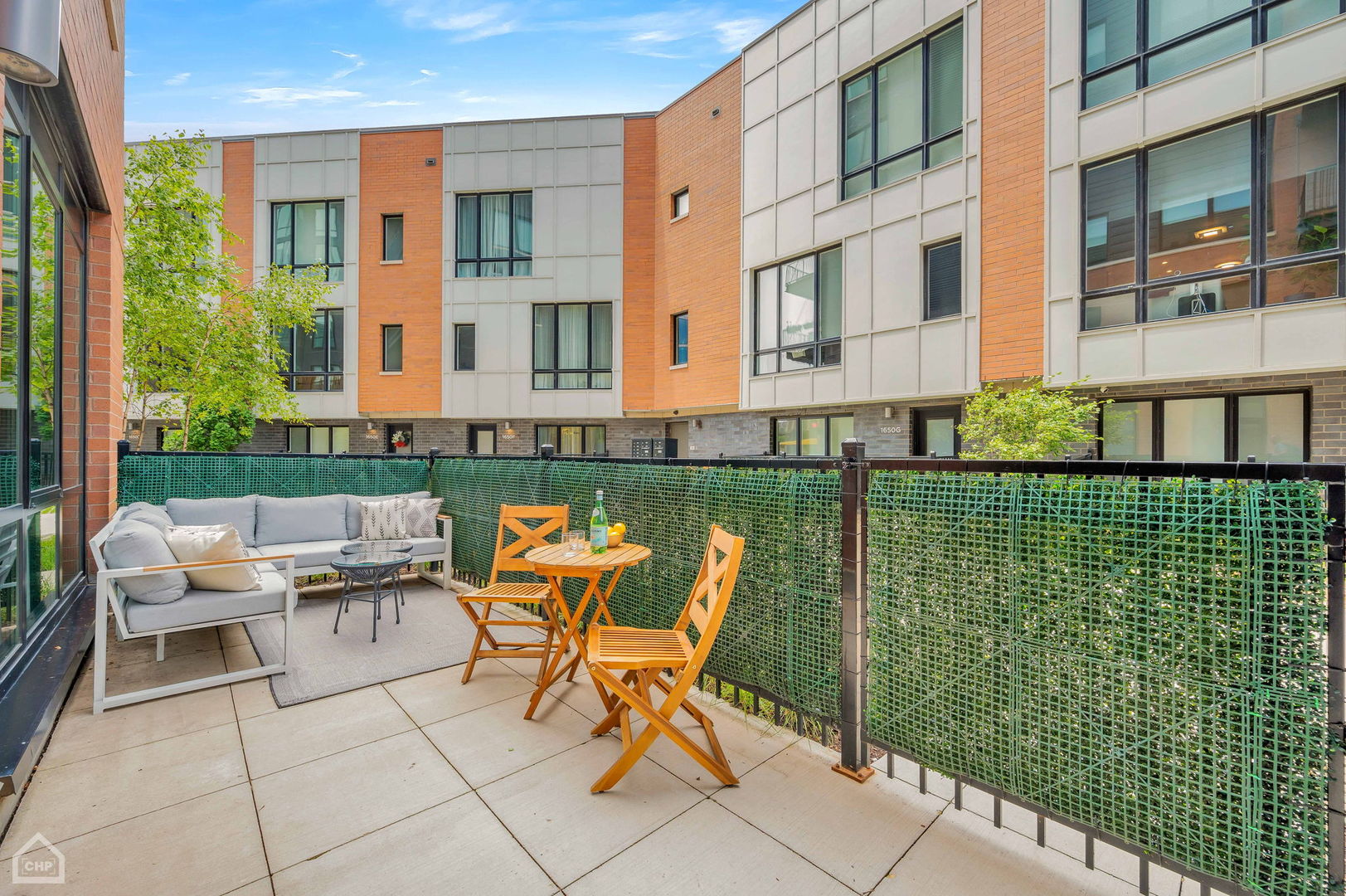 Furnished private patio with a gray sectional, wooden dining set, and view of a modern apartment building.