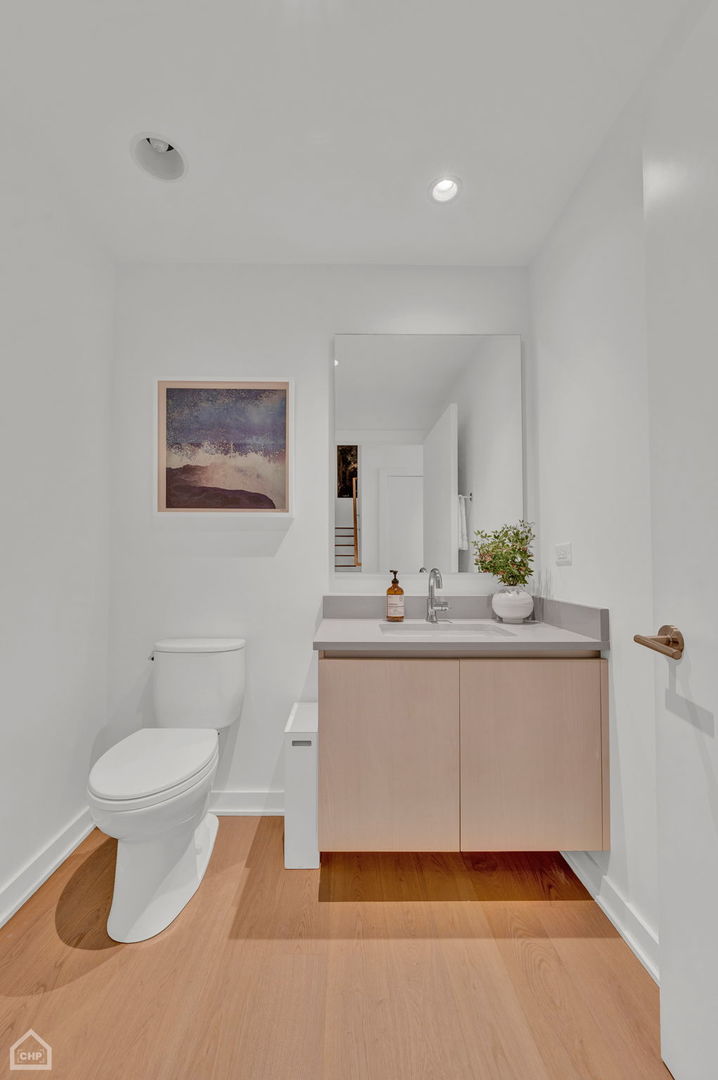Bathroom with a floating light-wood vanity, large mirror, white toilet, and warm wood flooring.