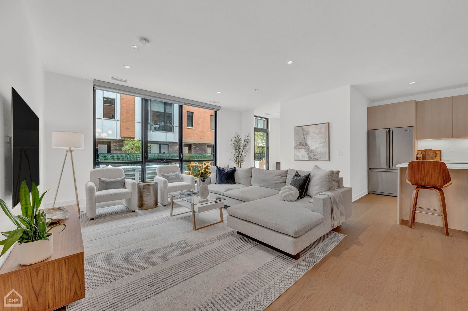 Living room with a large gray sectional, floor-to-ceiling windows, and an open kitchen.