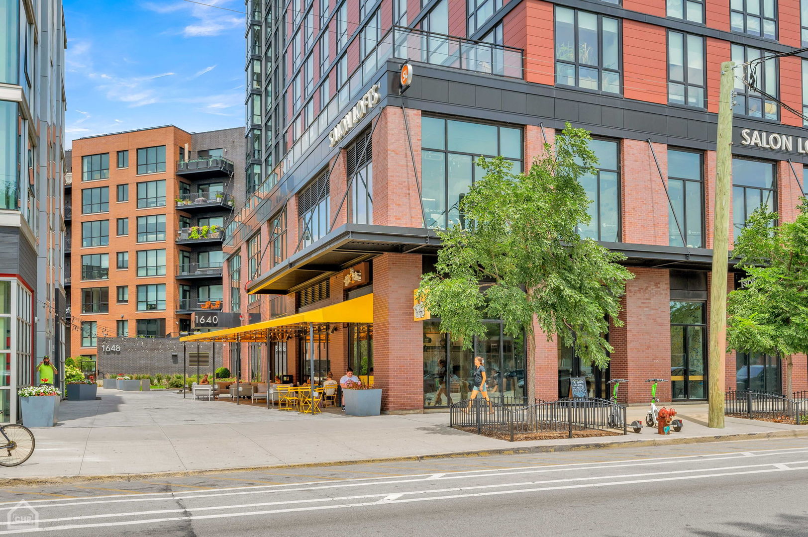 Modern brick and glass building with a yellow café awning and outdoor seating on Division Street.