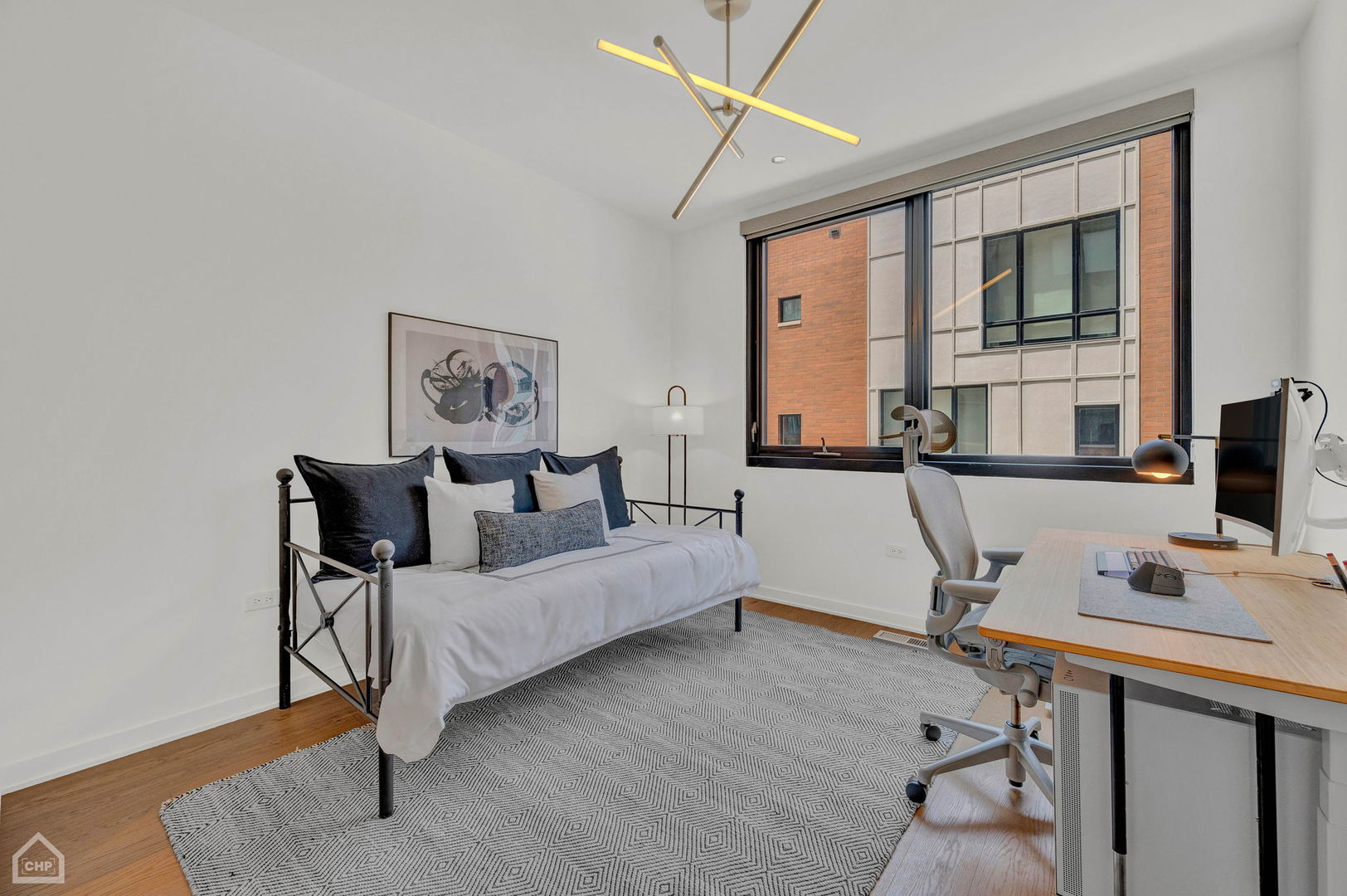 Staged bedroom and home office with a daybed and desk beside a large window.