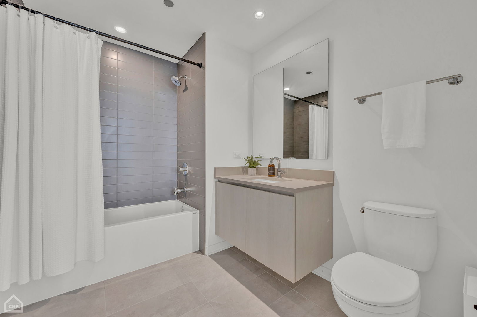 Modern bathroom with a tiled tub and shower, floating vanity, large mirror, and toilet.