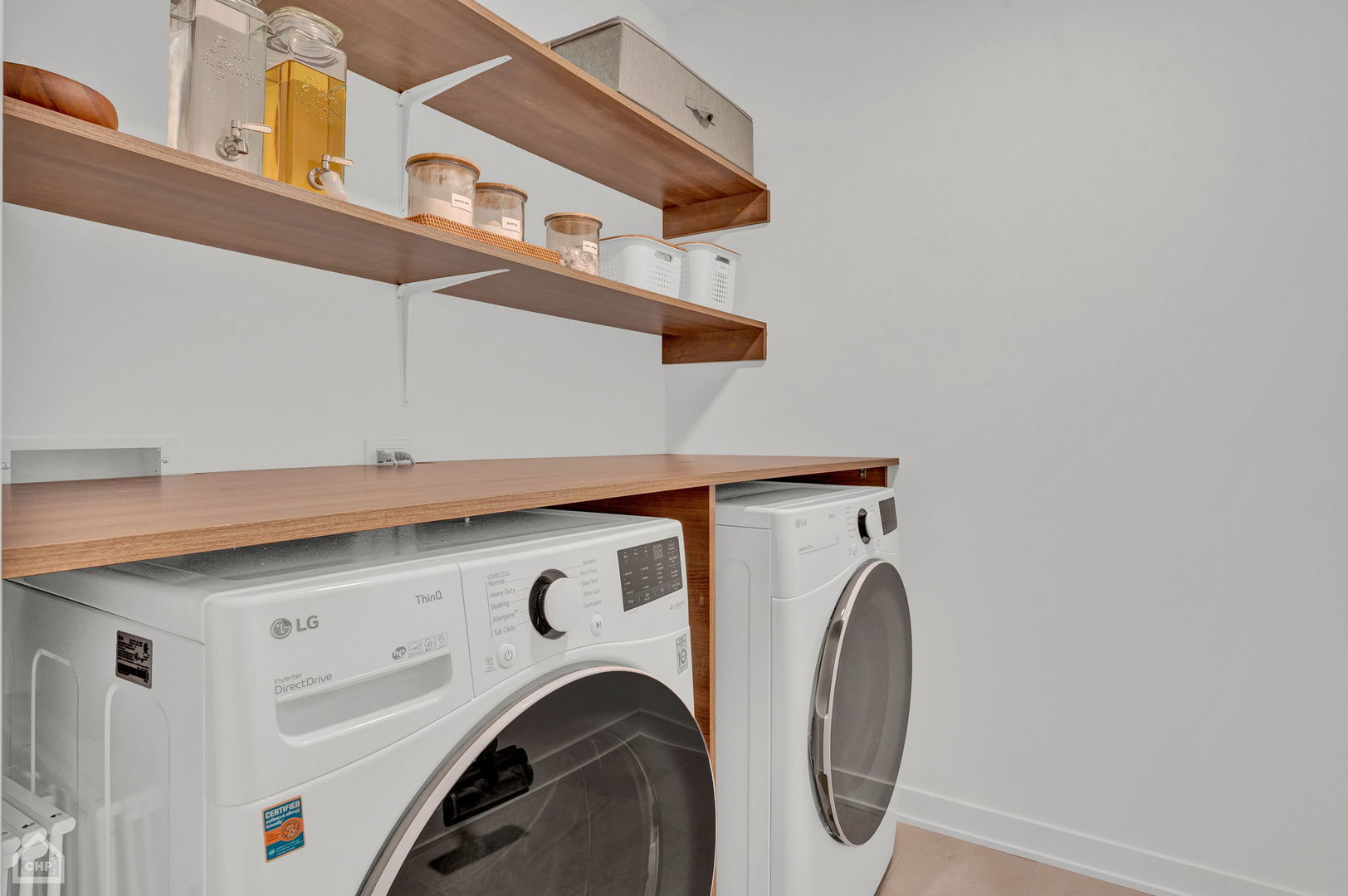 Laundry room with front-loading washer and dryer beneath a wood countertop and open storage shelves.