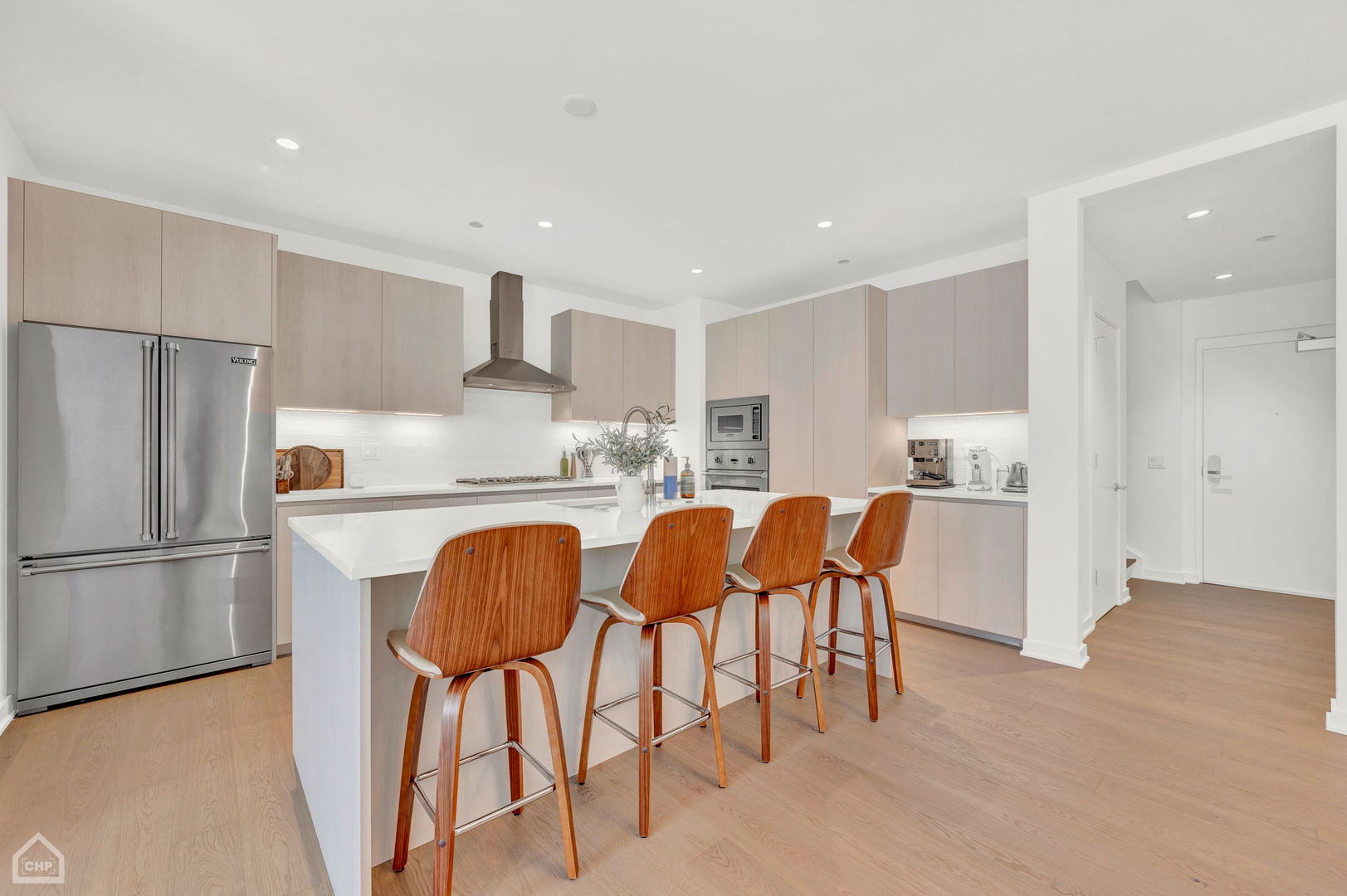 Modern condo kitchen with a white island, four wood bar stools, and stainless steel appliances.