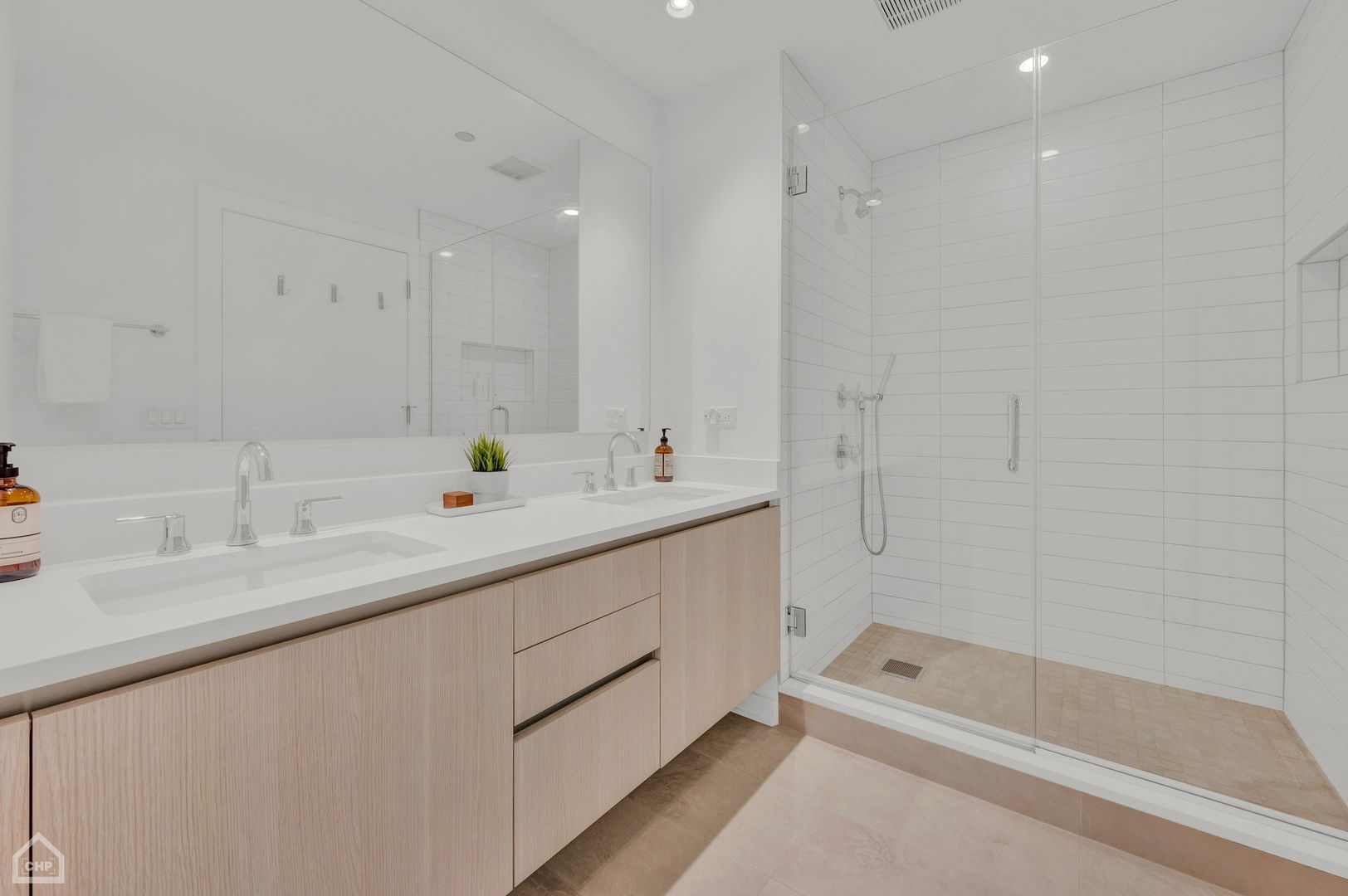 Modern bathroom with a double vanity and glass-enclosed, white-tiled shower.