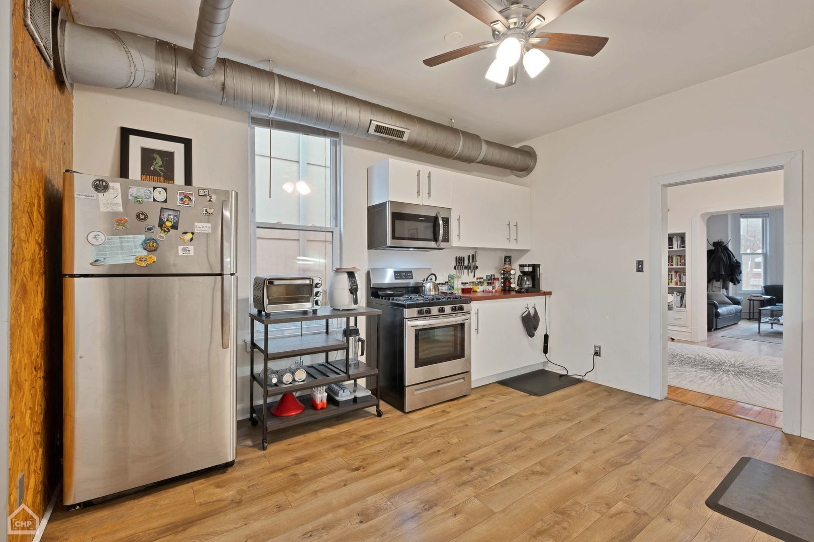 Kitchen with stainless steel appliances, white cabinets, exposed ceiling ductwork, and wood flooring.