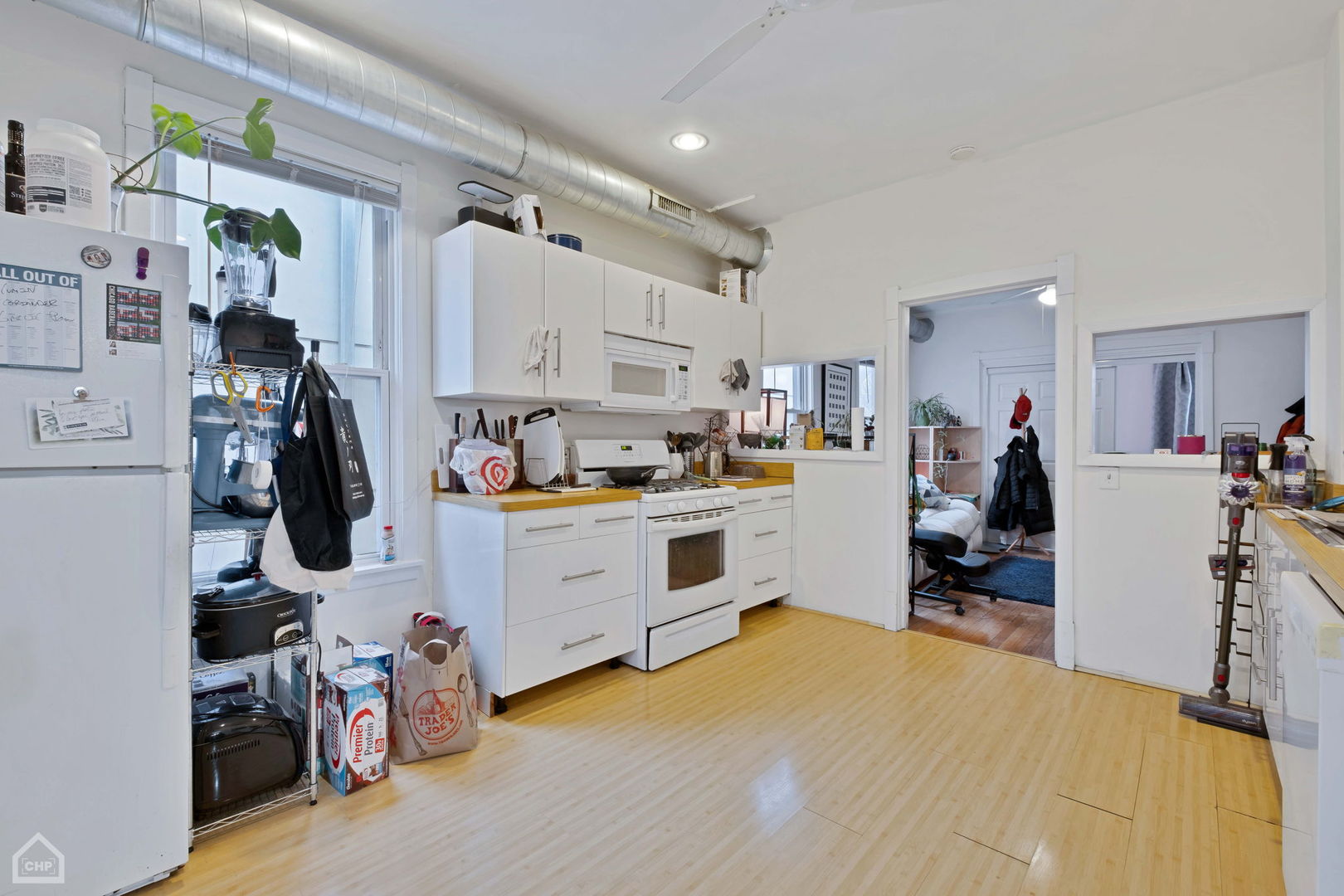 Kitchen with white cabinets, wood floors, and an exposed metal ceiling duct.