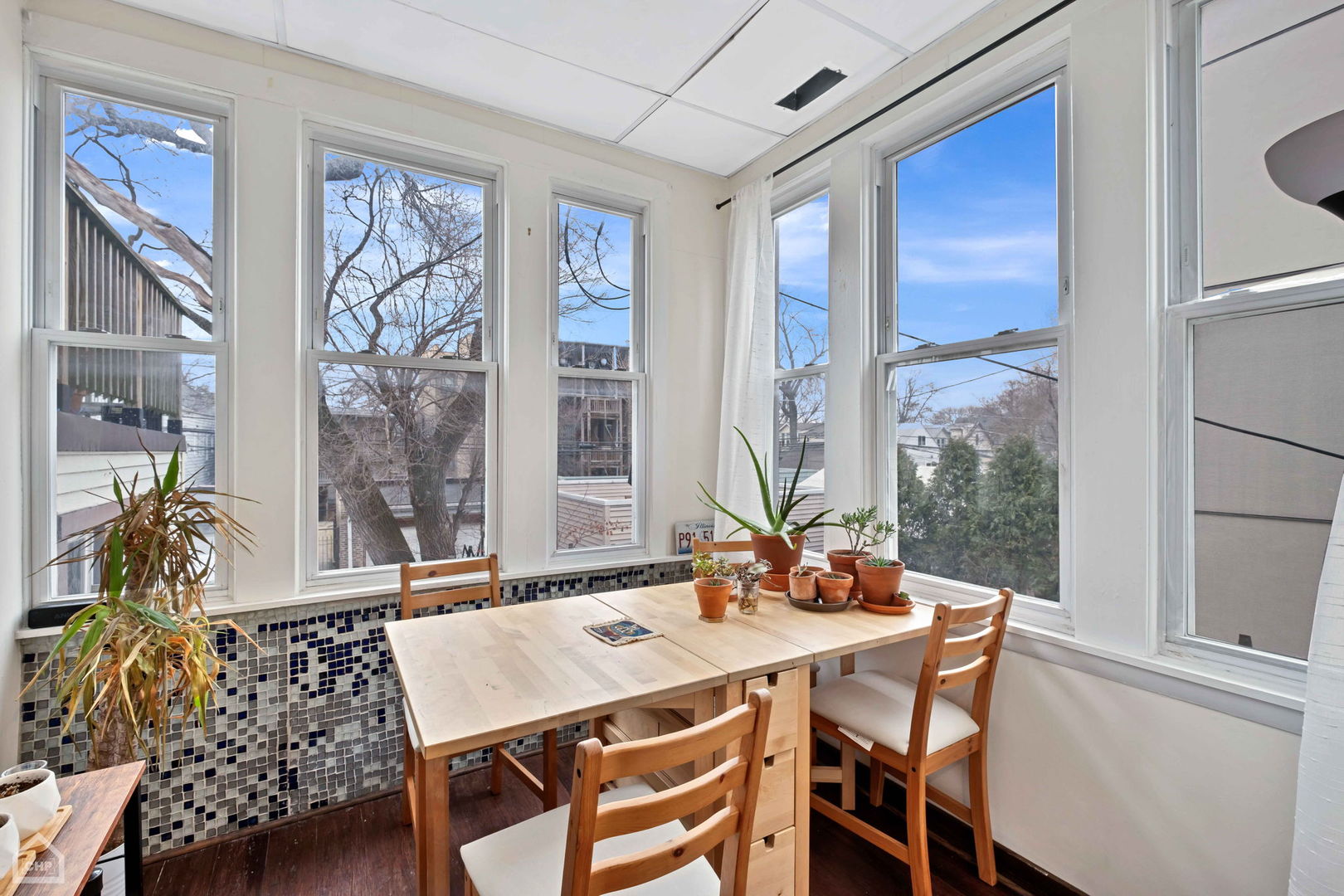Dining nook with a wooden table and chairs beside tall windows and a blue-and-white tile backsplash.