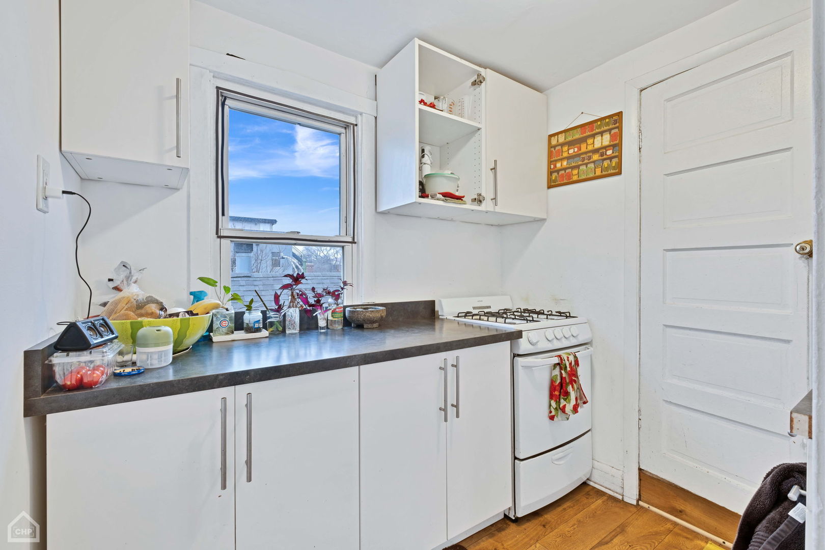 Kitchen with white cabinets, dark countertops, a gas range, and a window overlooking neighboring buildings.