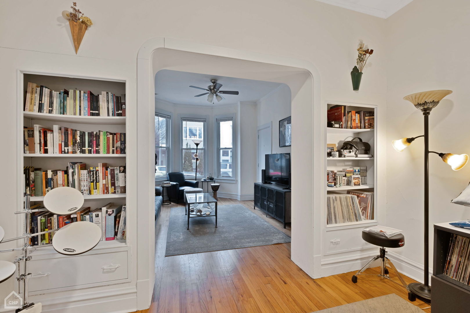 Living room with built-in bookcases, hardwood floors, and an arched opening to a bay-window seating area.
