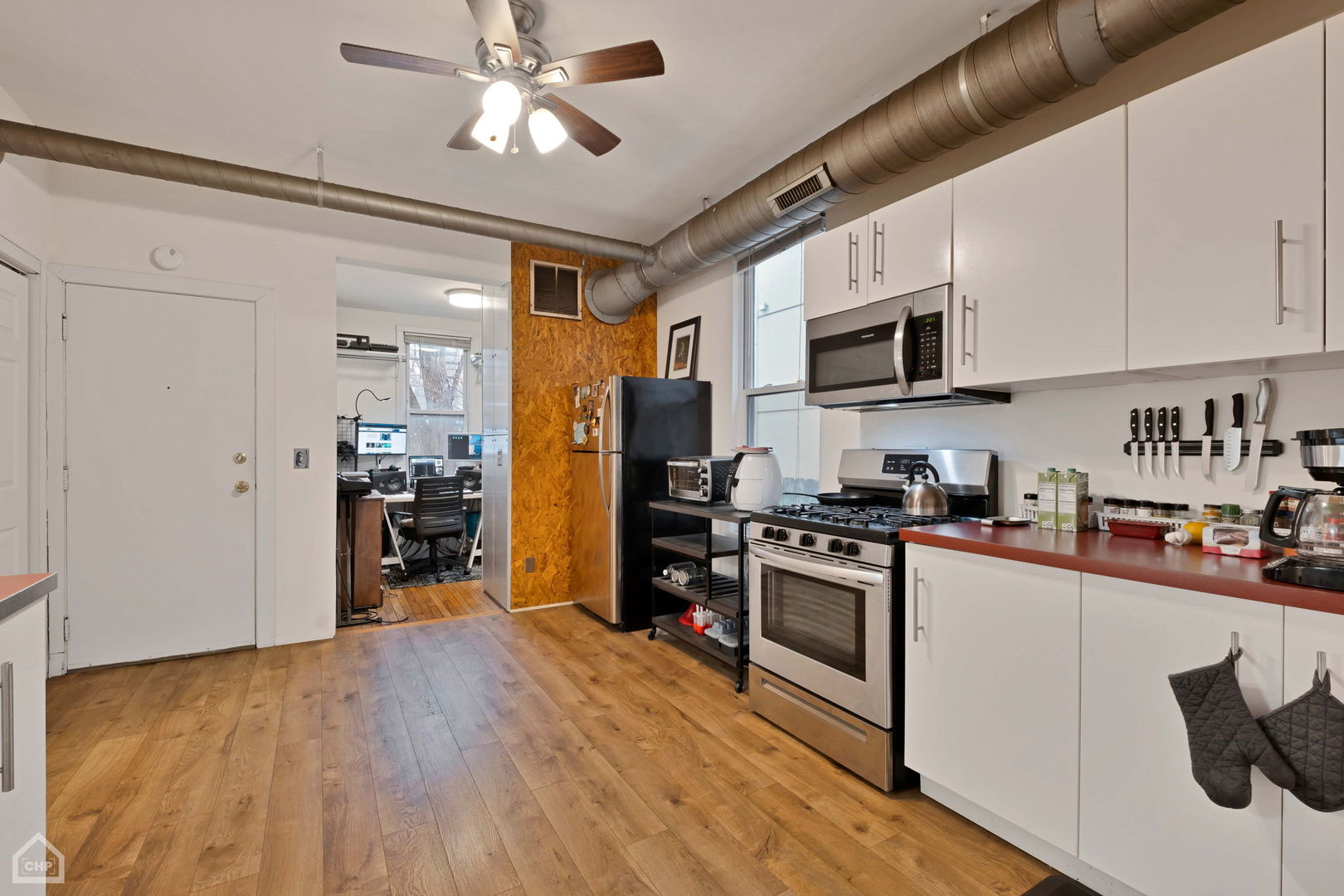 Kitchen with white cabinetry, stainless steel appliances, red countertop, and exposed ceiling ductwork.