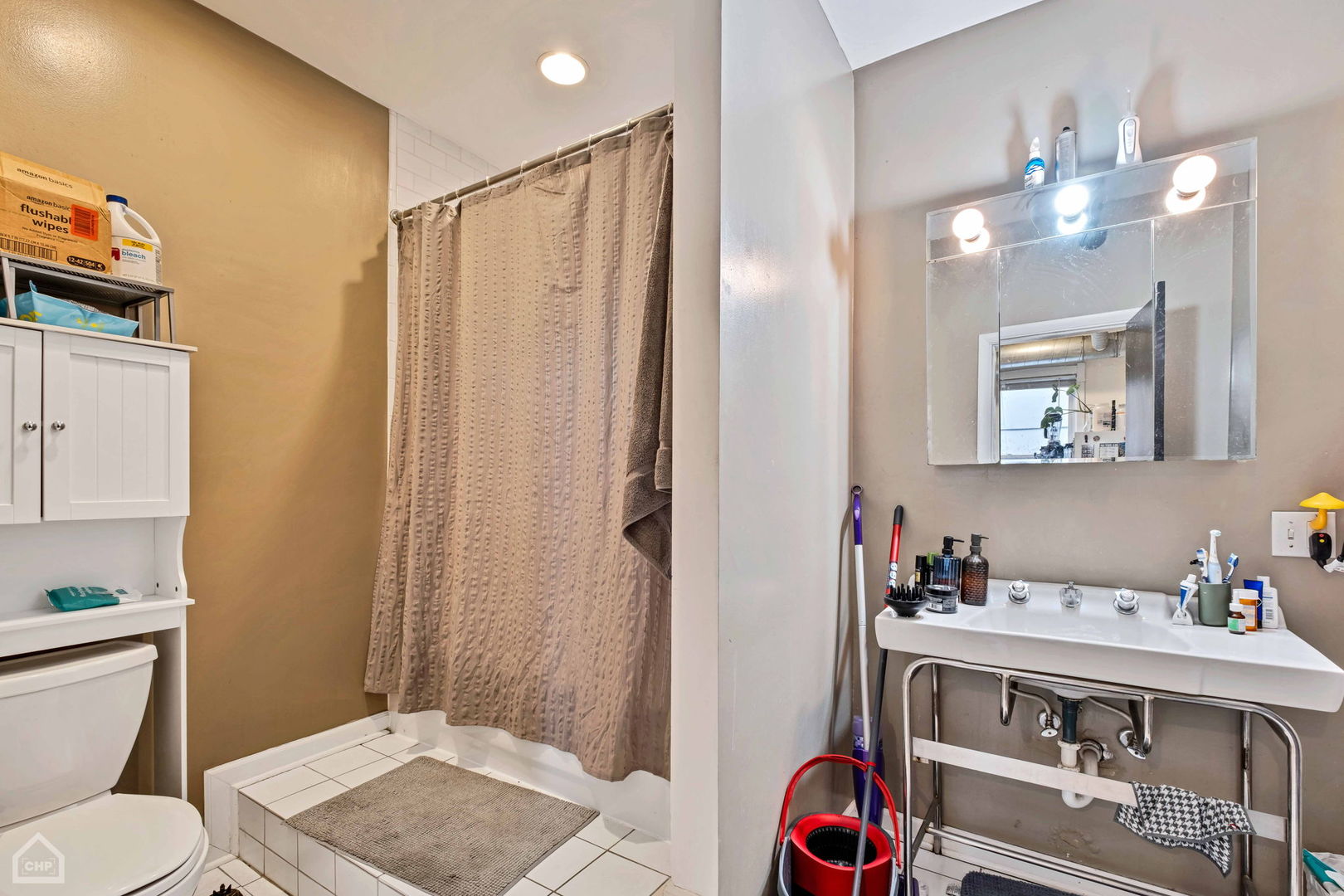 Bathroom with a tiled shower, beige curtain, toilet, and pedestal sink beneath a mirrored medicine cabinet.