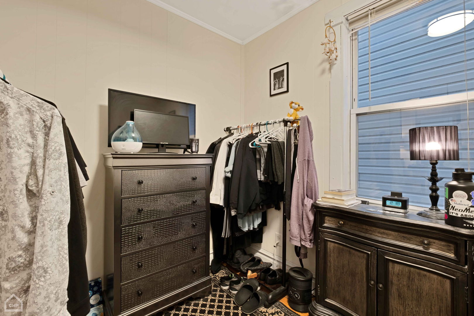 Furnished bedroom with a clothes rack, dark dresser, patterned rug, and large window.