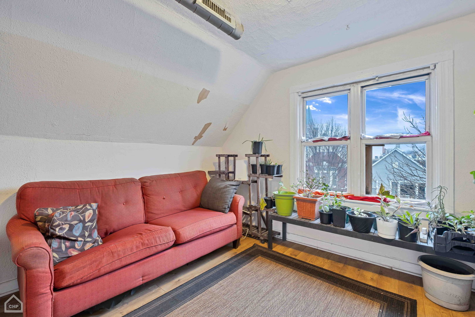 Attic sitting room with a red sofa, sloped ceiling, large windows, and potted plants.