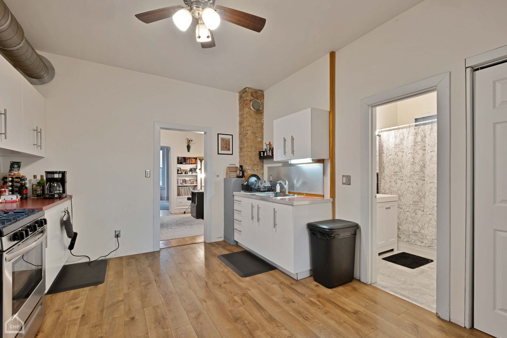 Kitchen with white cabinetry, wood floors, an exposed brick column, and an adjoining bathroom.