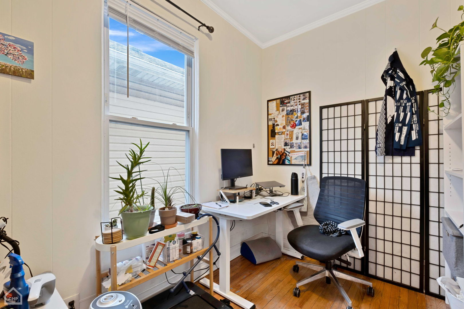 Home office with a white desk and rolling chair beside a large window with potted plants.