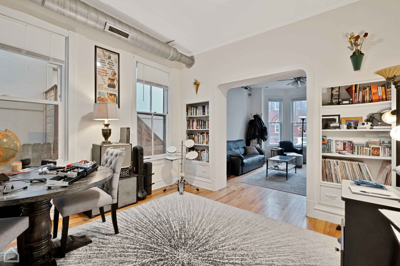 Furnished study with musical equipment and built-in bookshelves, opening to a living room with a blue sofa.